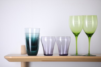 Photo of Empty clean glasses on wooden shelf near white wall indoors