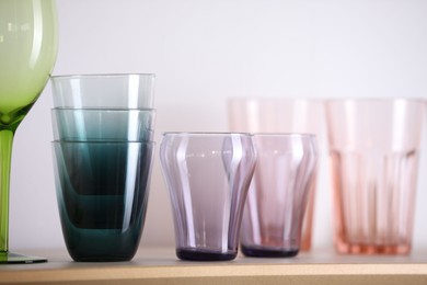 Photo of Empty clean glasses on wooden shelf near white wall indoors, closeup