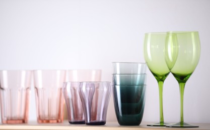 Photo of Empty clean glasses on wooden shelf near white wall indoors