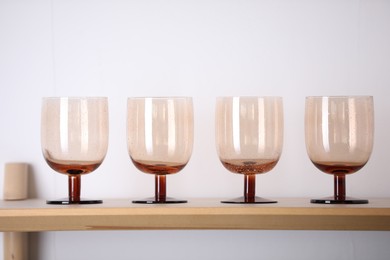 Photo of Empty clean glasses on wooden shelf near white wall indoors