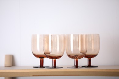 Photo of Empty clean glasses on wooden shelf near white wall indoors