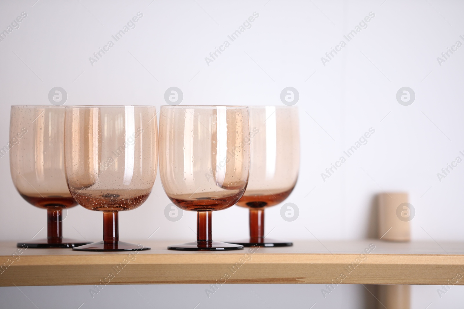 Photo of Empty clean glasses on wooden shelf near white wall indoors, space for text