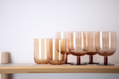 Photo of Empty clean glasses on wooden shelf near white wall indoors, space for text