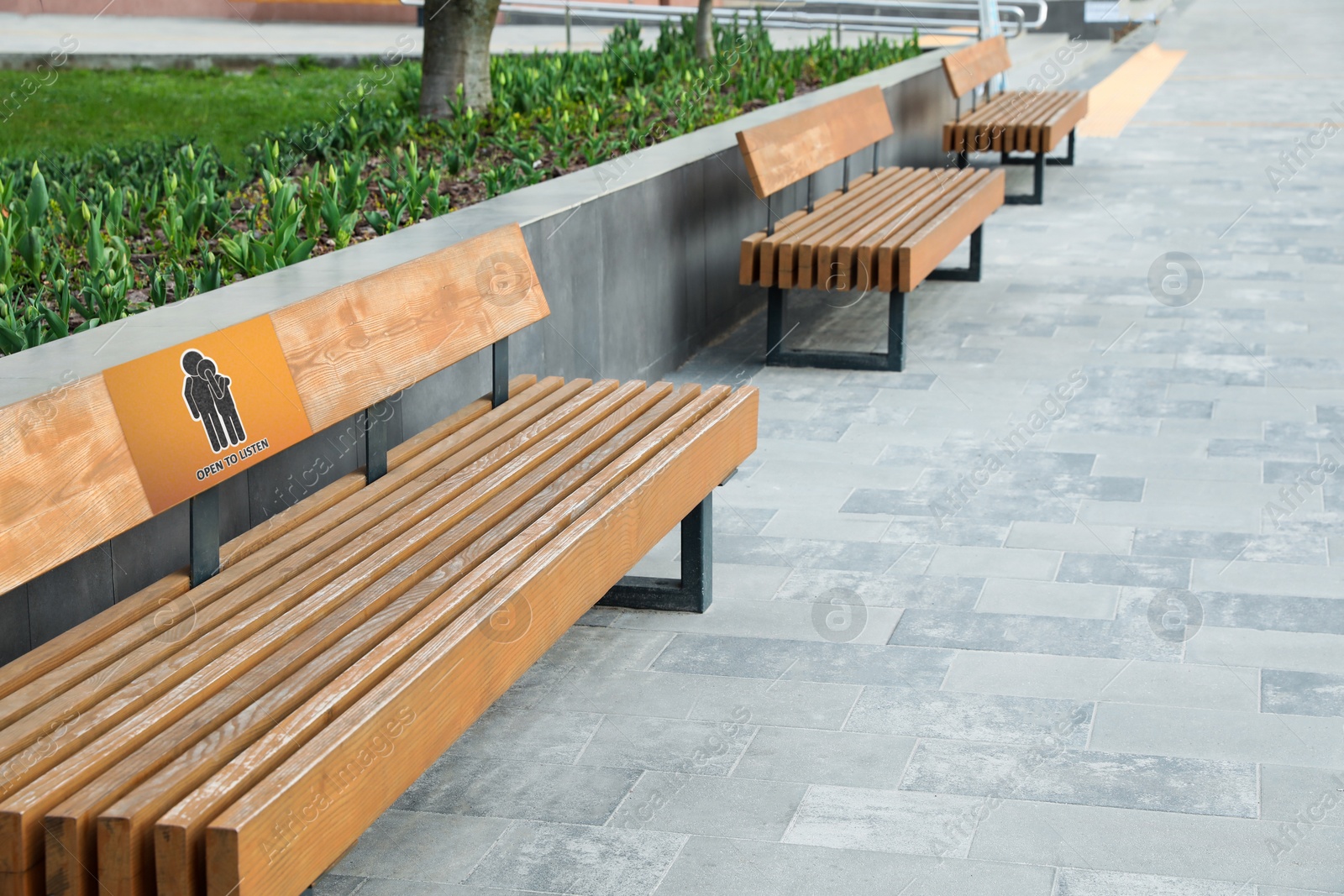 Image of Place where you can receive or give emotional support. Sign with human figures and text Open To Listen on bench outdoors