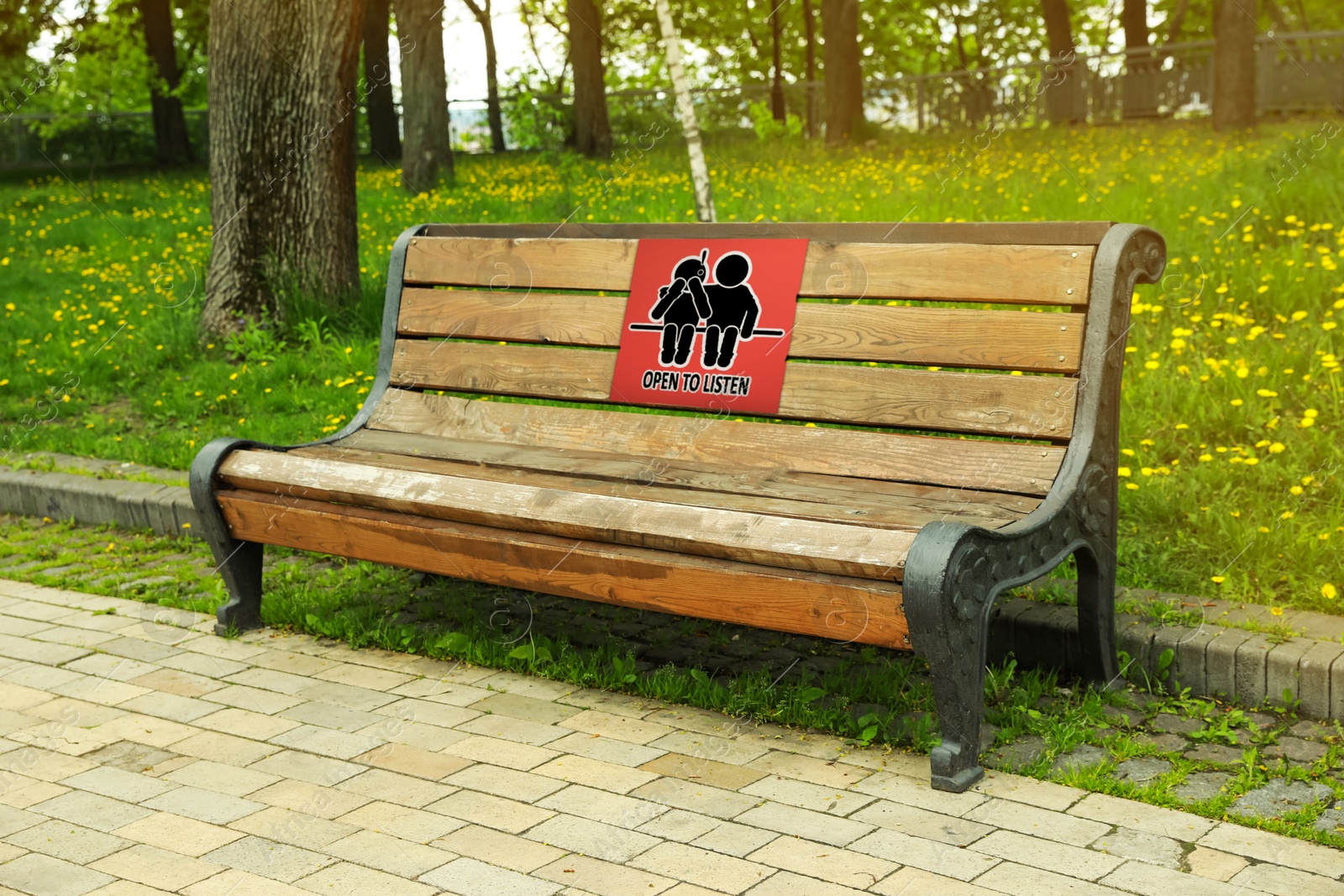 Image of Place where you can receive or give emotional support. Sign with human figures and text Open To Listen on bench outdoors