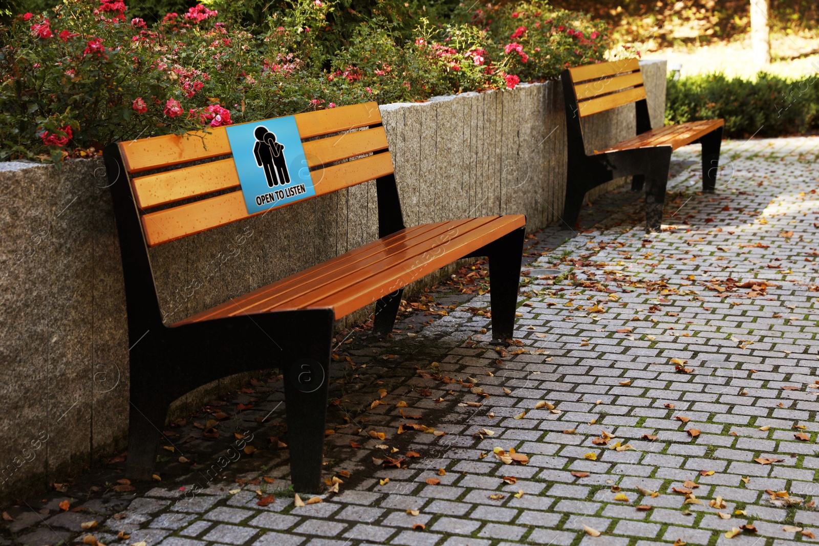 Image of Place where you can receive or give emotional support. Sign with human figures and text Open To Listen on bench outdoors