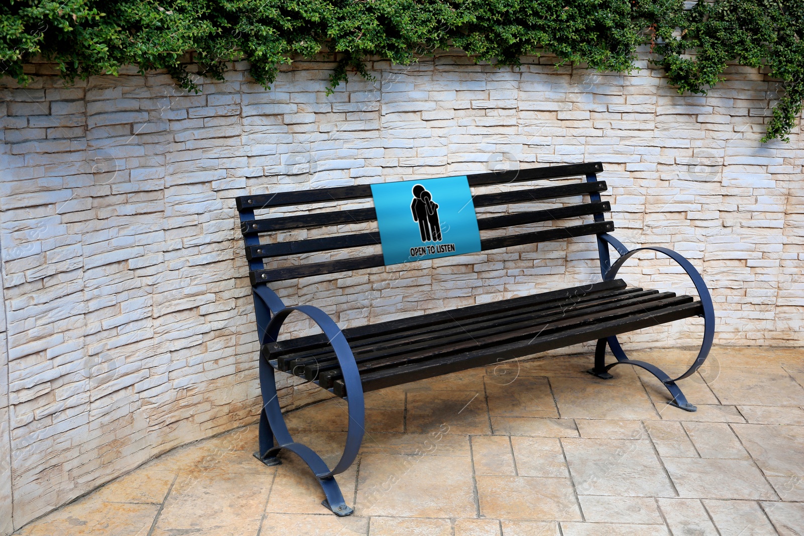 Image of Place where you can receive or give emotional support. Sign with human figures and text Open To Listen on bench outdoors