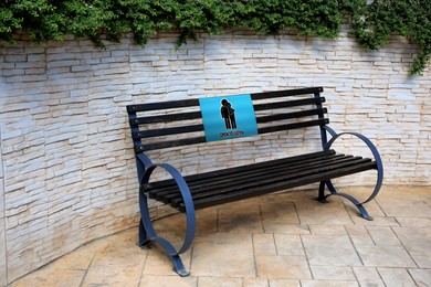 Image of Place where you can receive or give emotional support. Sign with human figures and text Open To Listen on bench outdoors