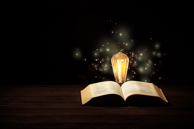 Image of Glowing light bulb and book on wooden table