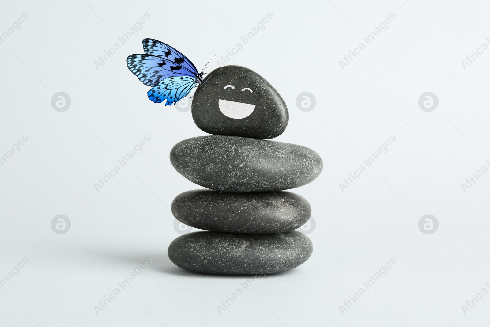 Image of Butterfly on stone with smiling face, stack of pebbles on white background. Harmony