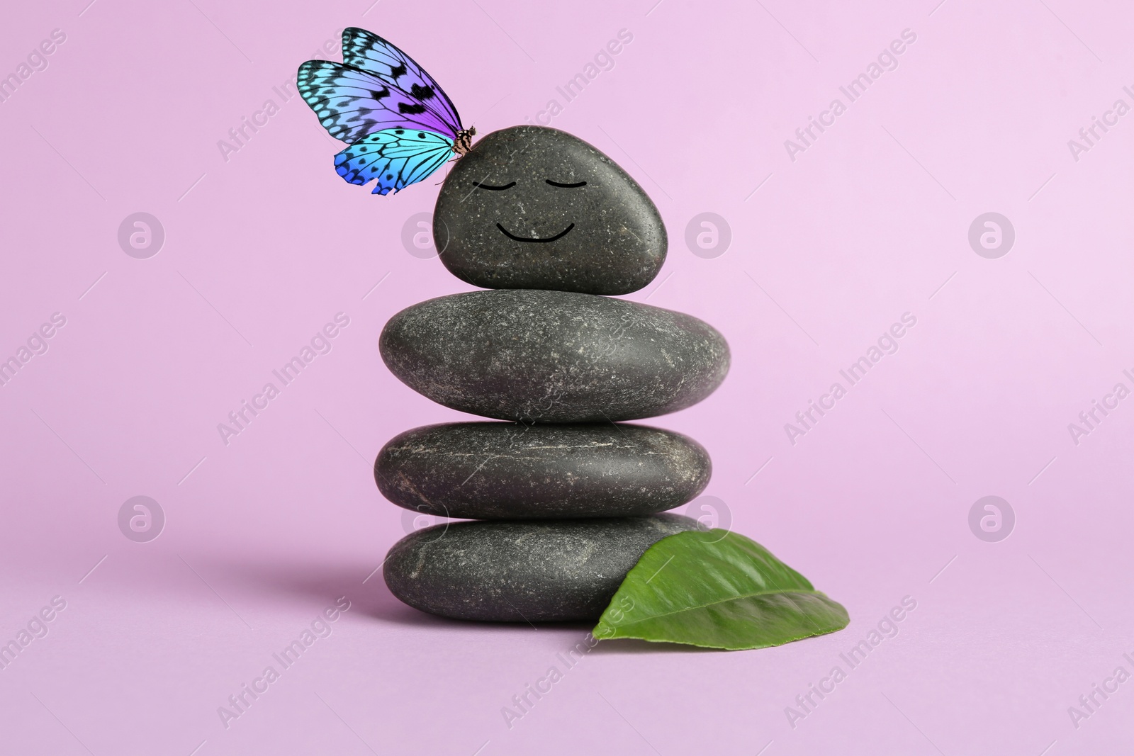 Image of Butterfly on stone with smiling face, stack of pebbles and green leaf on light violet background. Harmony