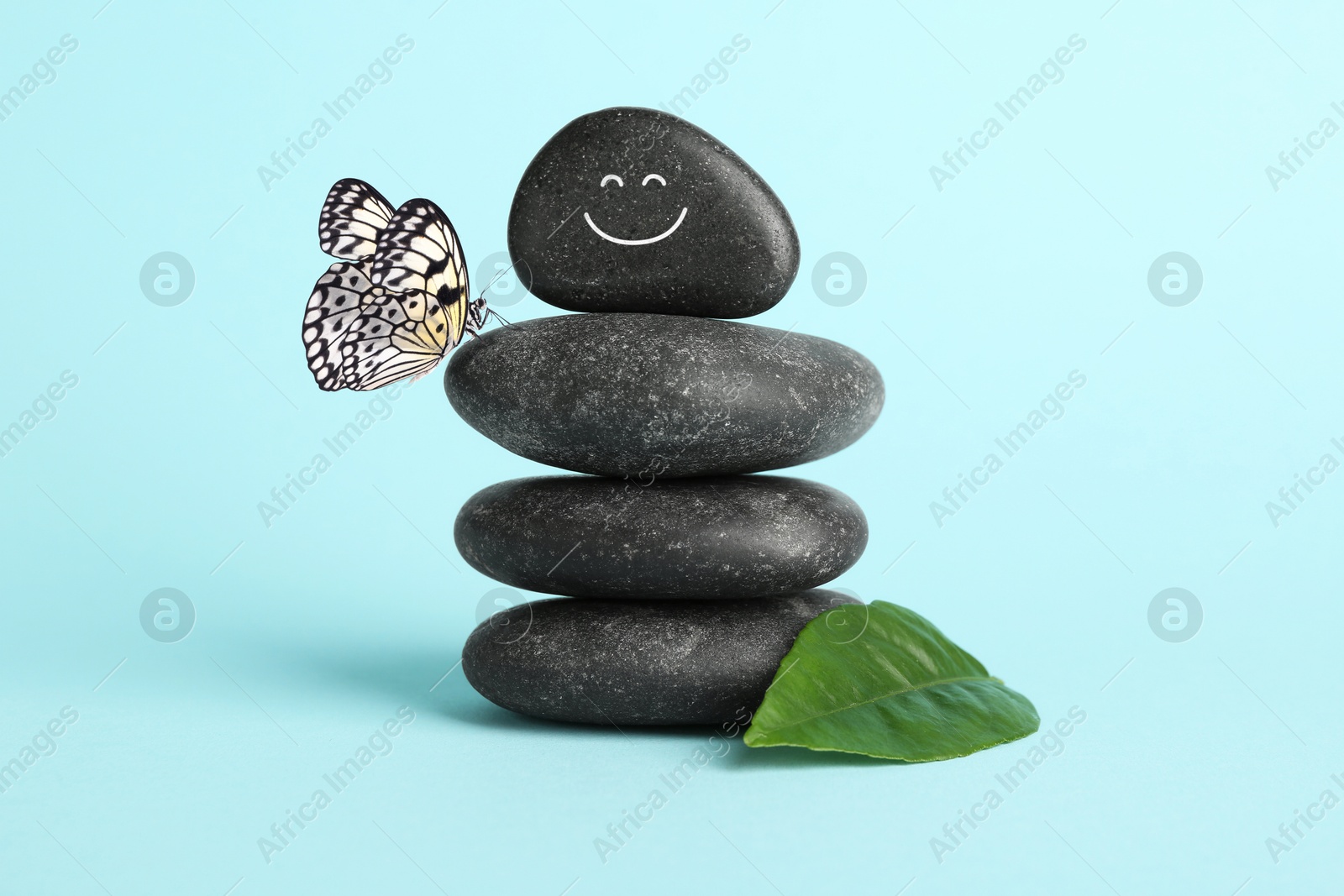 Image of Happy stone glad to see butterfly, harmony. Stacked pebbles and one with smiling face on top against light turquoise background