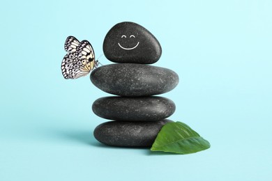 Image of Happy stone glad to see butterfly, harmony. Stacked pebbles and one with smiling face on top against light turquoise background