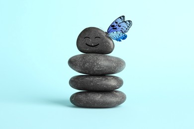 Image of Butterfly on stone with smiling face, stack of pebbles on light blue background. Harmony