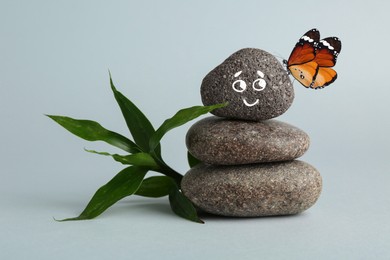 Image of Happy stone glad to see butterfly, harmony. Stacked pebbles and one with smiling face on top against grey background