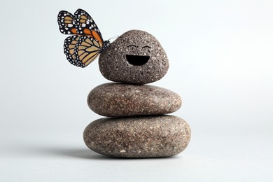 Image of Butterfly on stone with smiling face, stack of pebbles on white background. Harmony