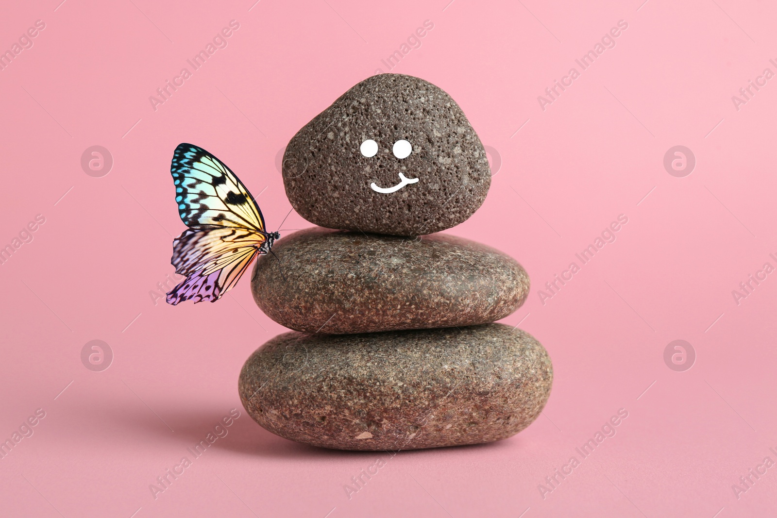 Image of Happy stone glad to see butterfly, harmony. Stacked pebbles and one with smiling face on top against pink background