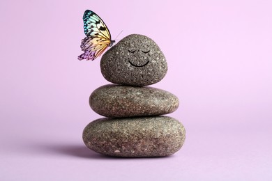 Image of Butterfly on stone with smiling face, stack of pebbles on light violet background. Harmony