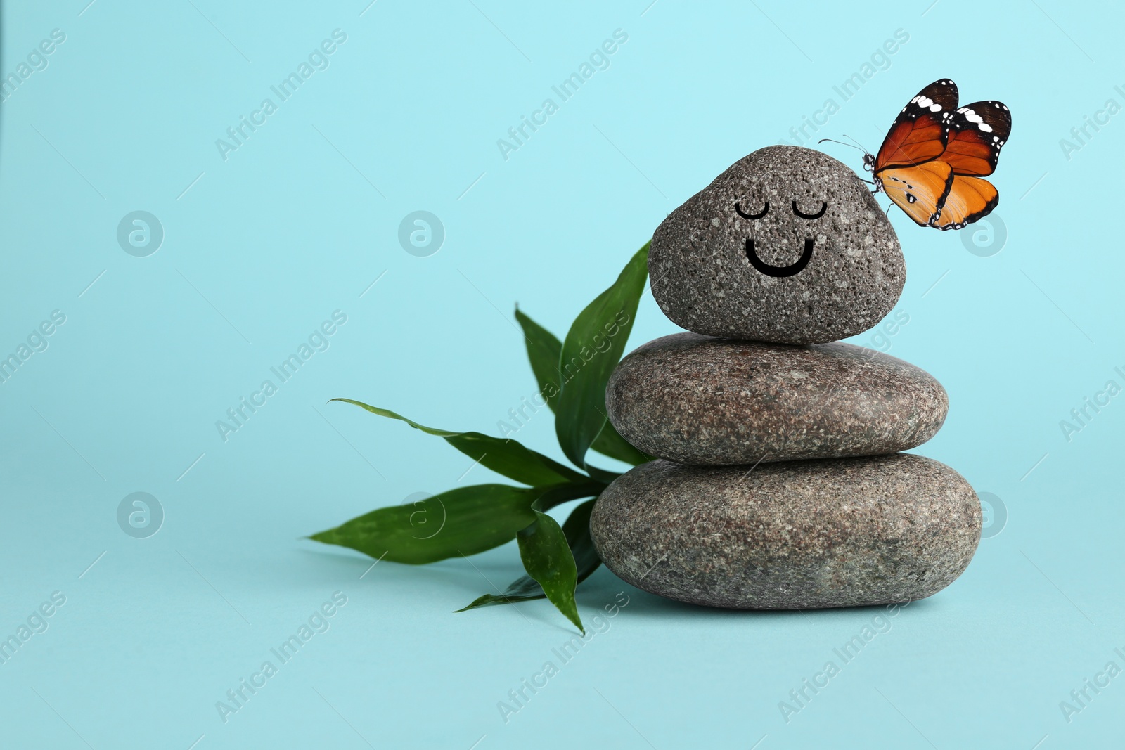 Image of Butterfly on stone with smiling face, stack of pebbles and green branch on light blue background, space for text. Harmony