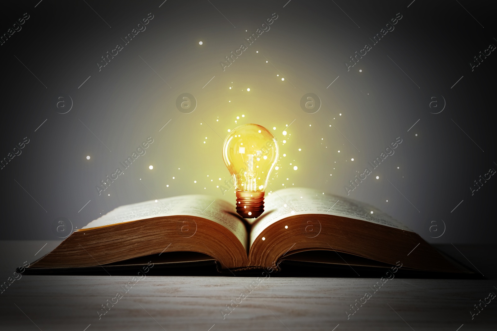 Image of Book with glowing light bulb on wooden table and magic lights