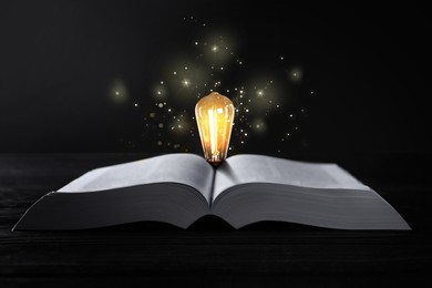 Image of Book and glowing light bulb on wooden table