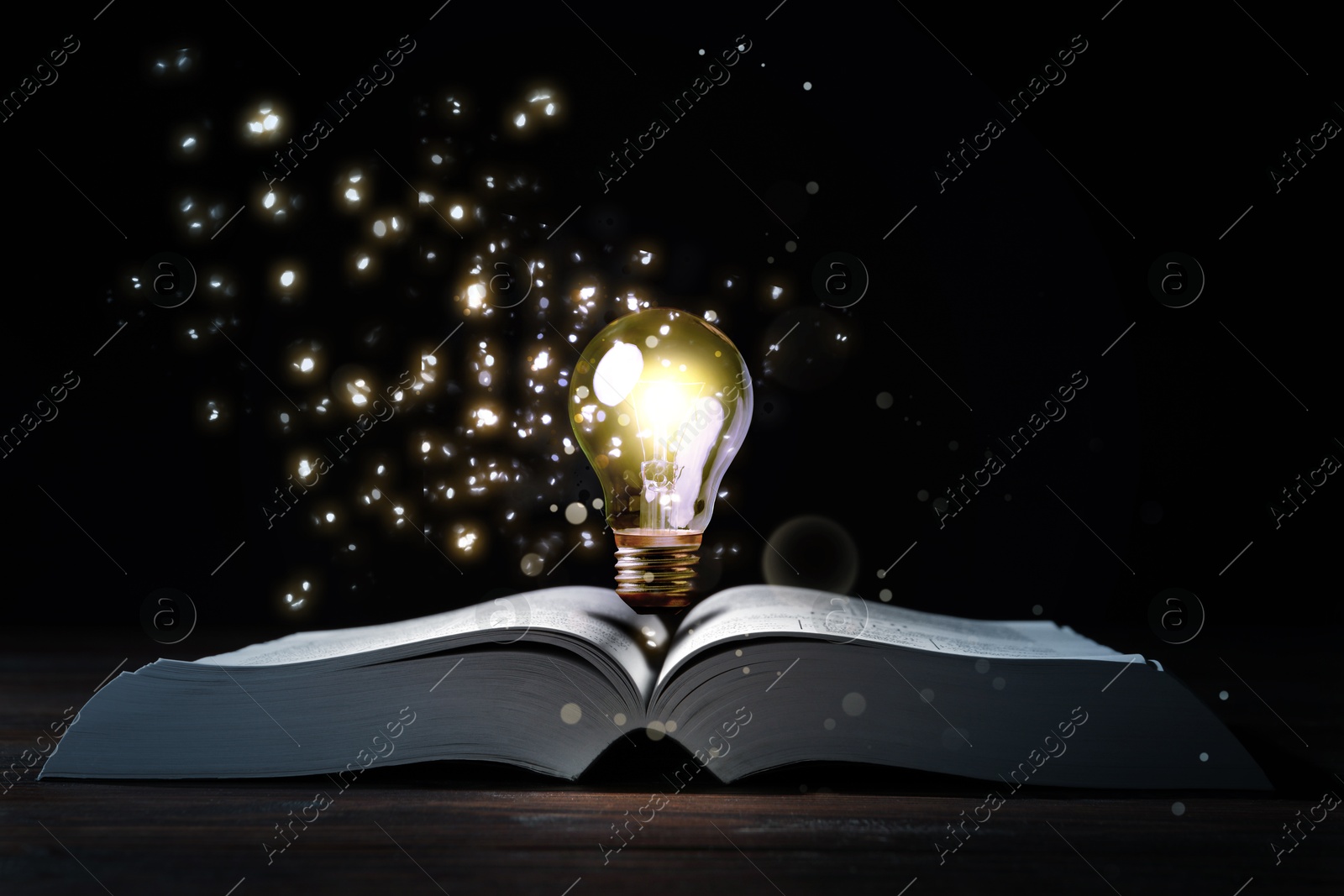 Image of Book with glowing light bulb on wooden table and magic lights