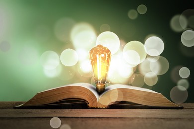 Image of Book with glowing light bulb on wooden table, bokeh lights