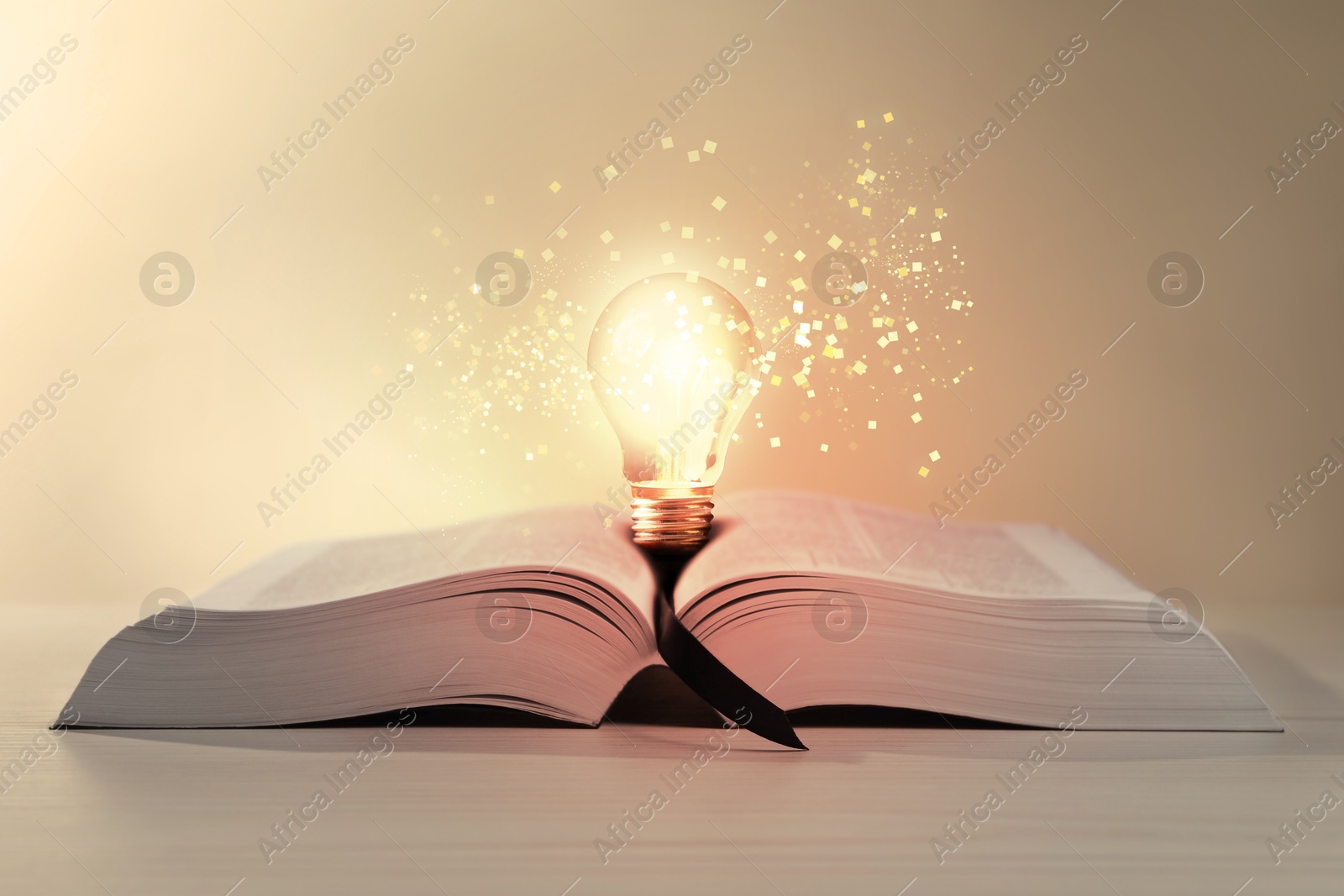 Image of Book with glowing light bulb on wooden table and magic lights