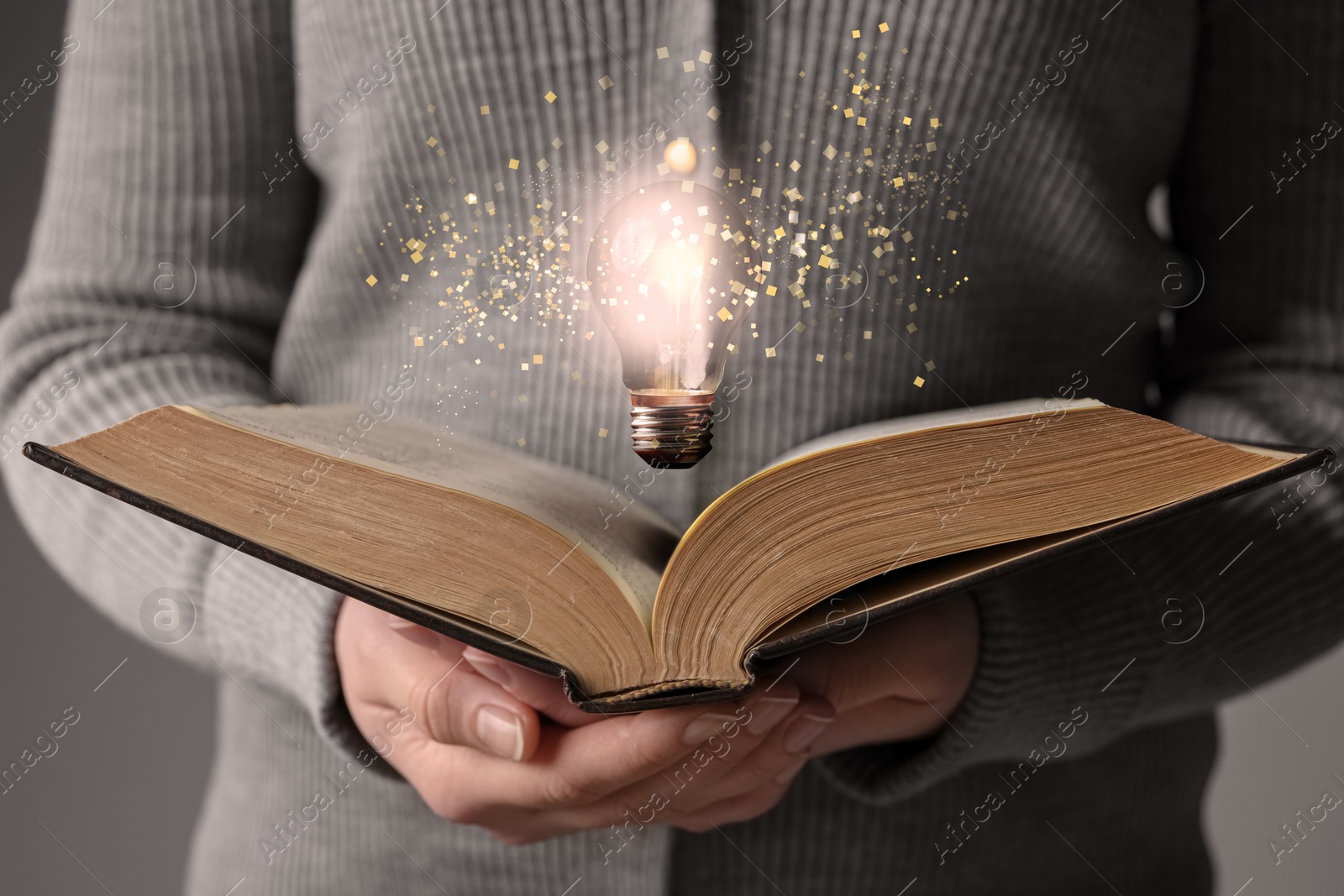 Image of Woman holding book, closeup. Glowing light bulb and magic sparks over pages