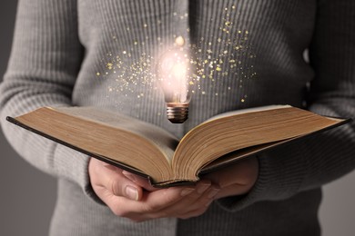 Image of Woman holding book, closeup. Glowing light bulb and magic sparks over pages