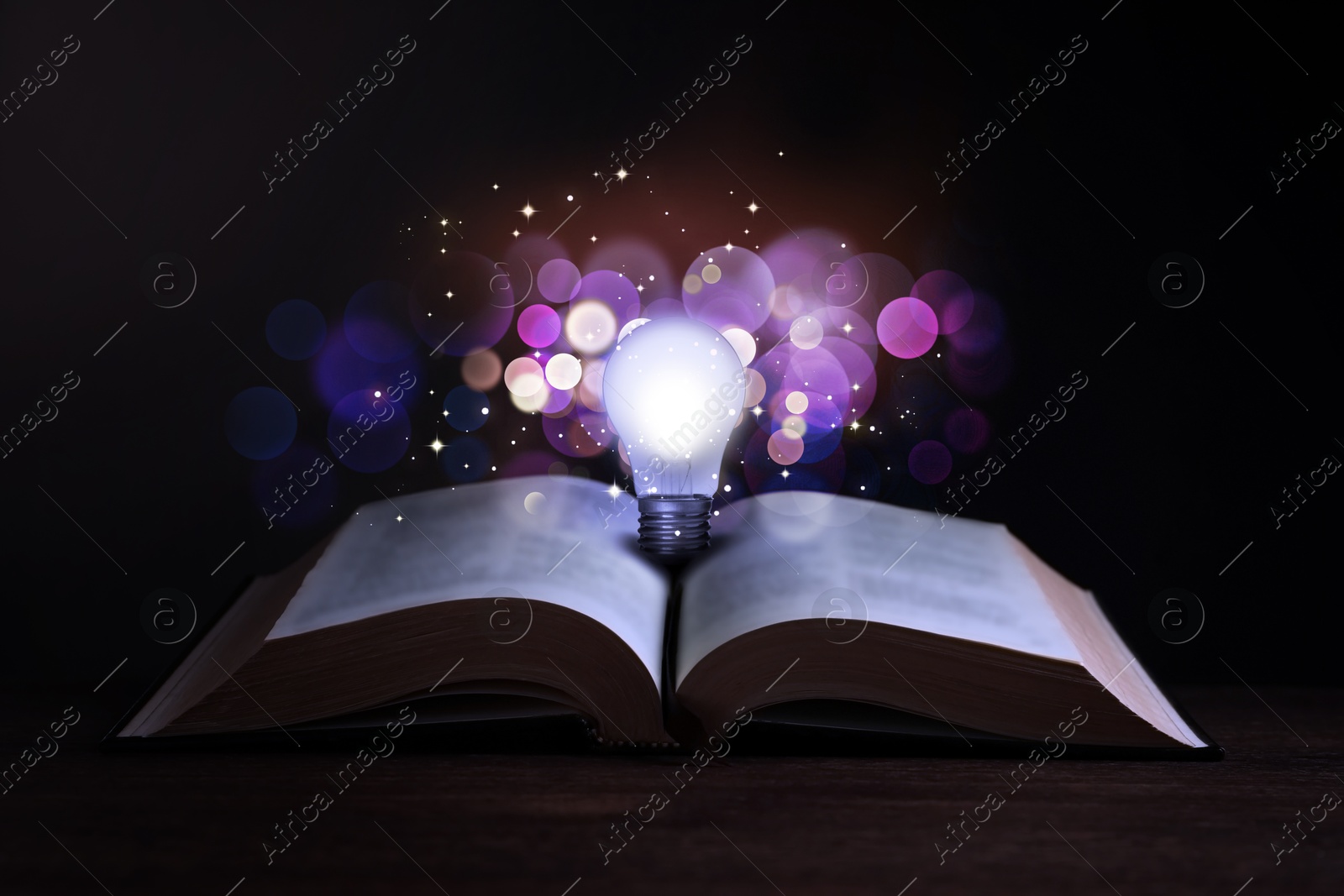 Image of Book with glowing light bulb on wooden table and magic lights