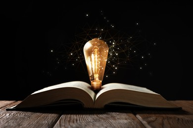 Image of Book with glowing light bulb on wooden table and magic lights