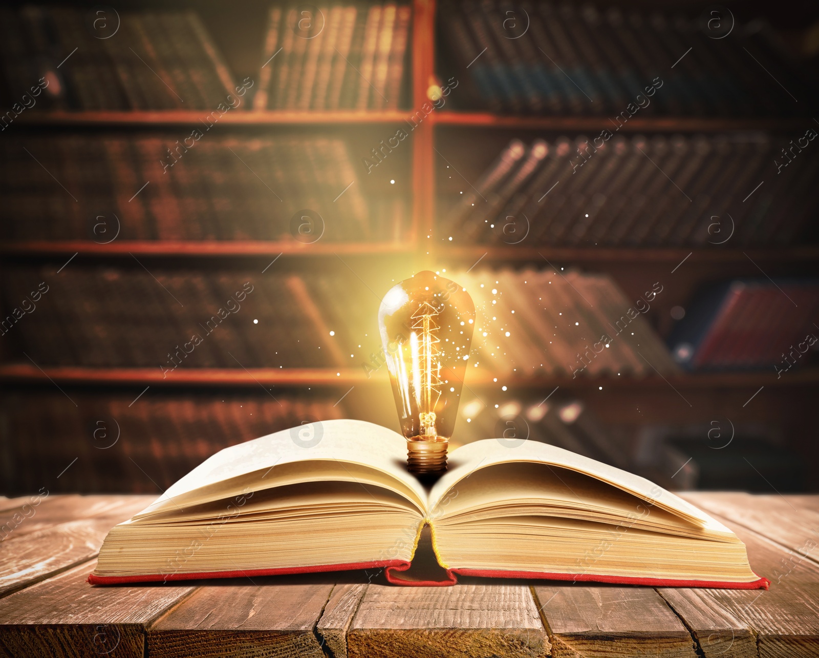 Image of Book with glowing light bulb on wooden table and magic lights in library