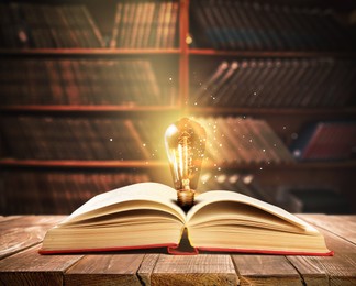 Image of Book with glowing light bulb on wooden table and magic lights in library