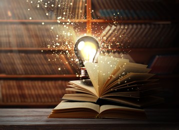 Image of Books and glowing light bulb on wooden table in library