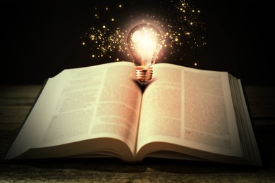 Image of Book with glowing light bulb on wooden table and magic lights