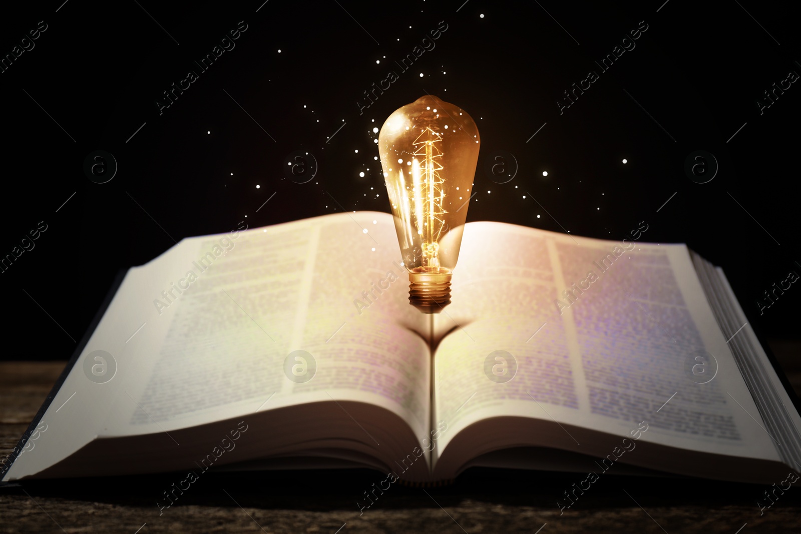 Image of Glowing light bulb in air over book on wooden table and magic lights