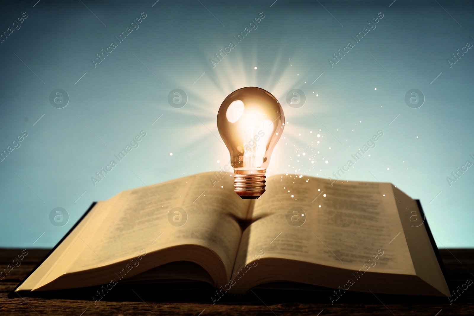 Image of Glowing light bulb in air over book on wooden table and magic lights