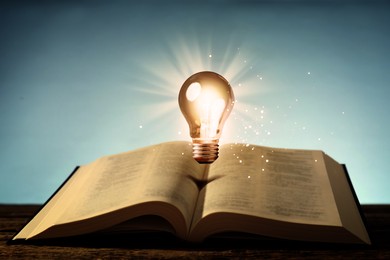 Image of Glowing light bulb in air over book on wooden table and magic lights