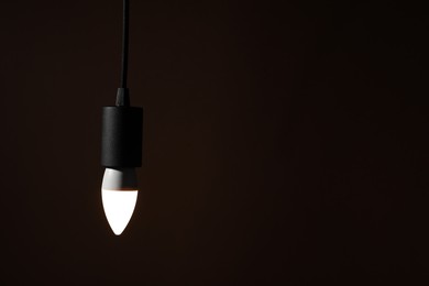 Photo of Glowing light bulb hanging on dark background. Space for text