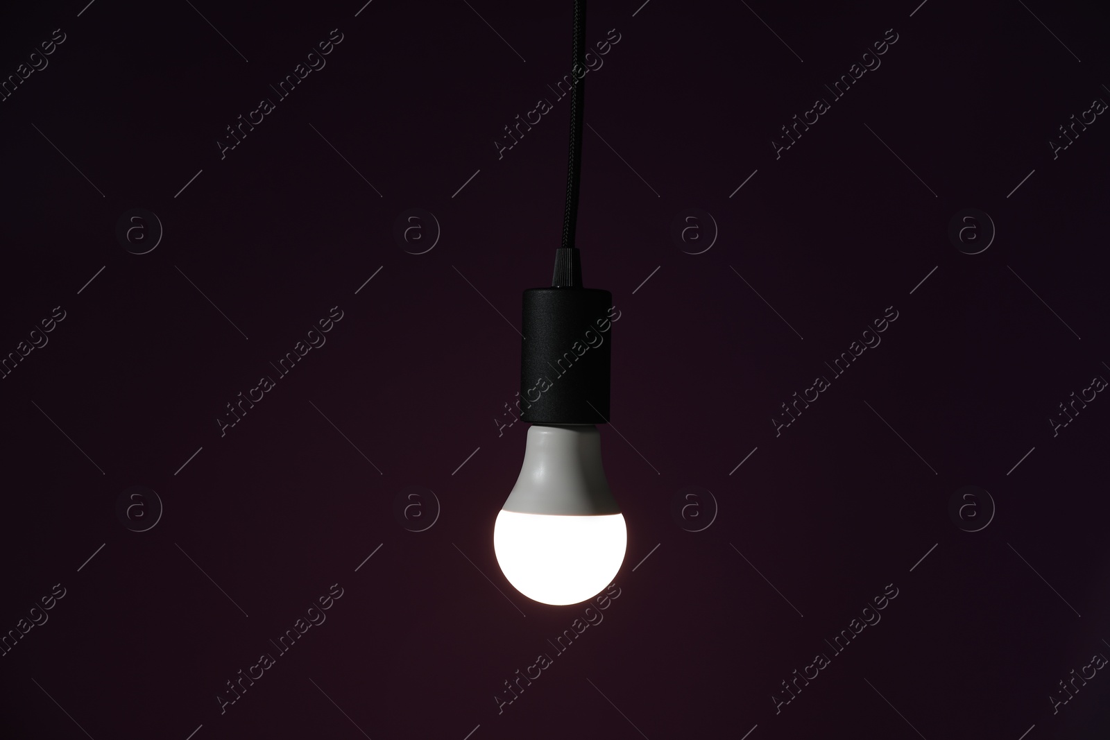 Photo of Glowing light bulb hanging on dark purple background