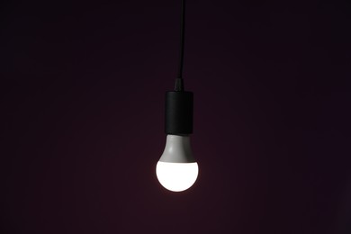 Photo of Glowing light bulb hanging on dark purple background