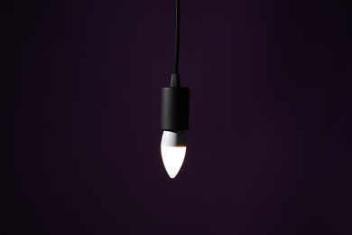 Photo of Glowing light bulb hanging on dark purple background