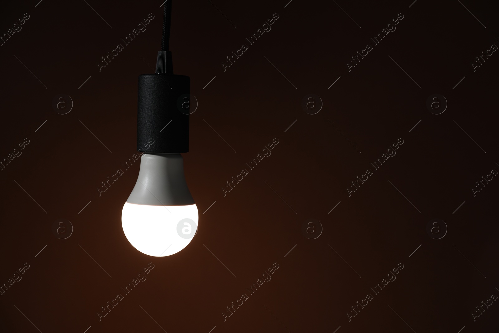 Photo of Glowing light bulb hanging on dark background. Space for text