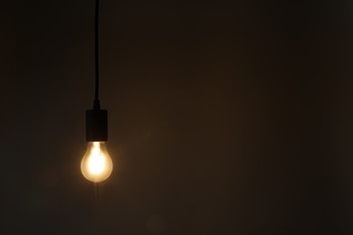 Photo of Glowing light bulb hanging on dark background. Space for text