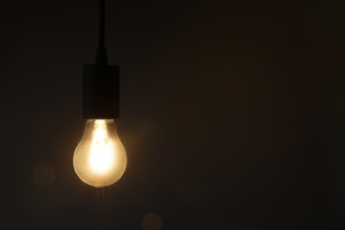 Photo of Glowing light bulb hanging on dark background. Space for text