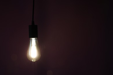 Photo of Glowing light bulb hanging on dark purple background. Space for text