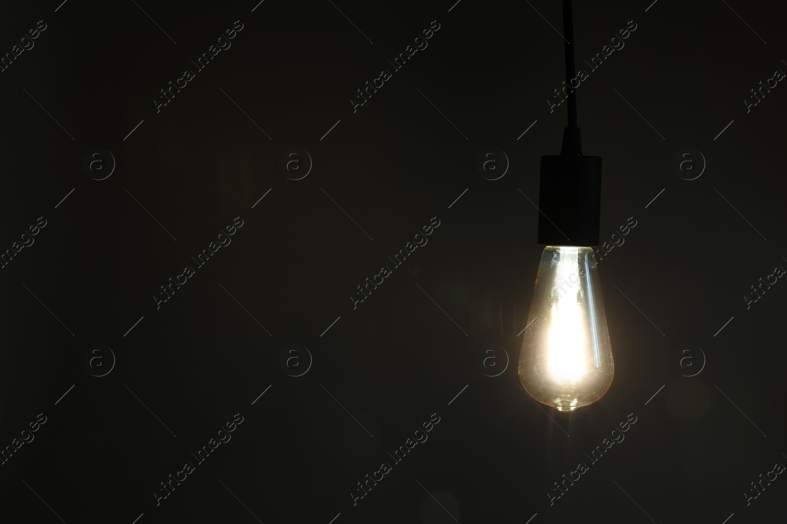 Photo of Glowing light bulb hanging on dark background. Space for text