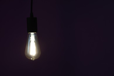 Photo of Glowing light bulb hanging on dark purple background. Space for text