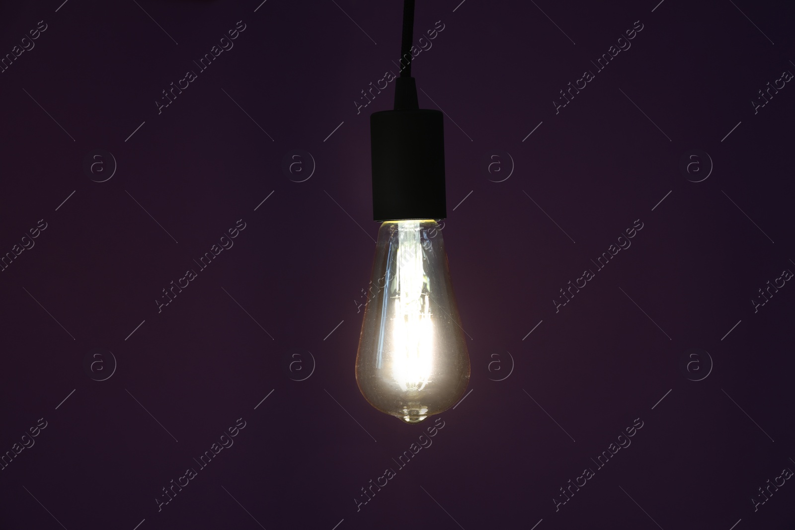 Photo of Glowing light bulb hanging on dark purple background